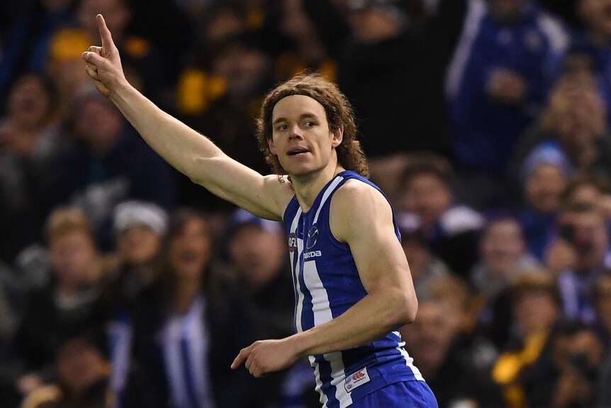 A male AFL player raises a finger on his right hand to celebrate kicking a goal.