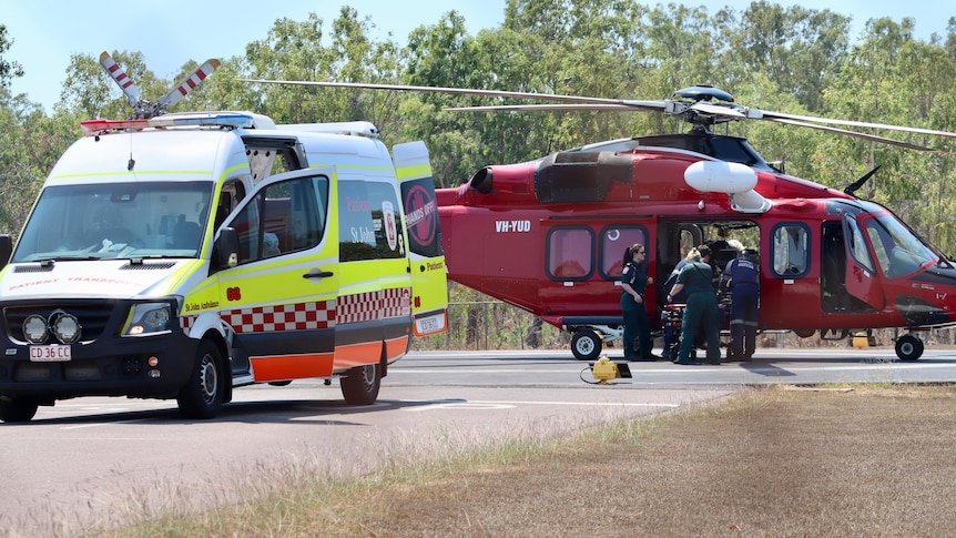 An ambulance and a helicopter are in a strip of runway with paramedics working.