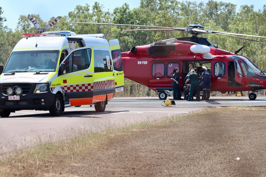 An ambulance and a helicopter are in a strip of runway with paramedics working.