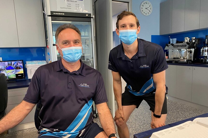 Two men wearing at the reception desk of an indoor pool