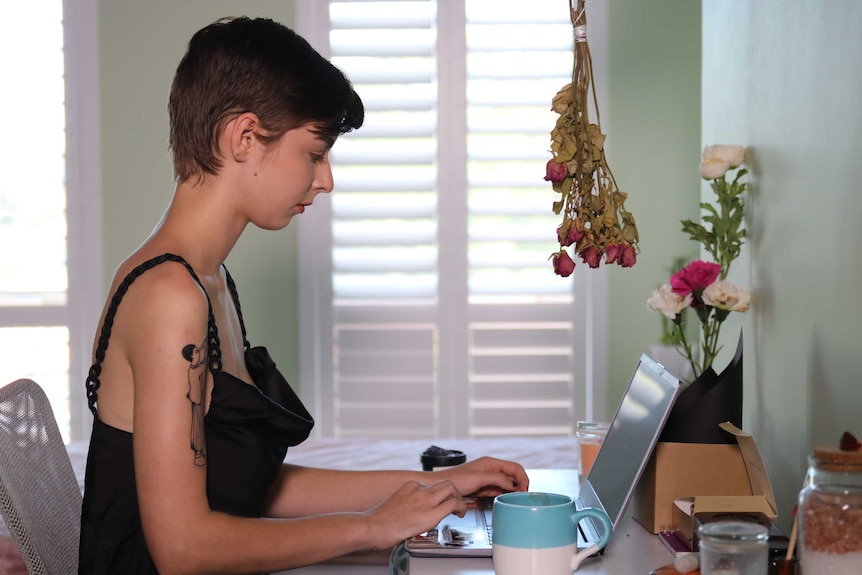 A woman with short hair sits at a laptop computer inside a home