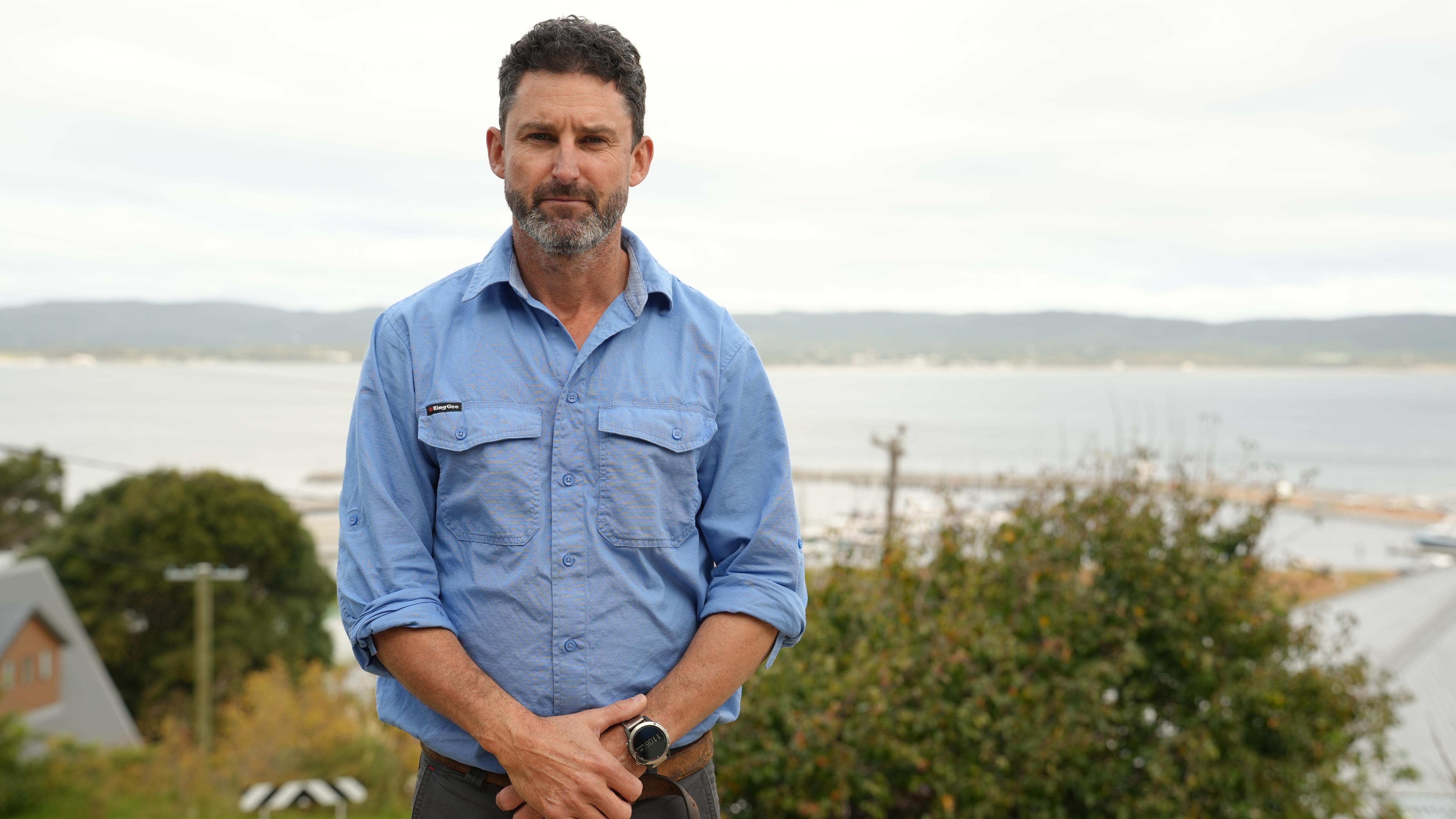 A man with hands crossed in front of him and ocean in background looking at camera.