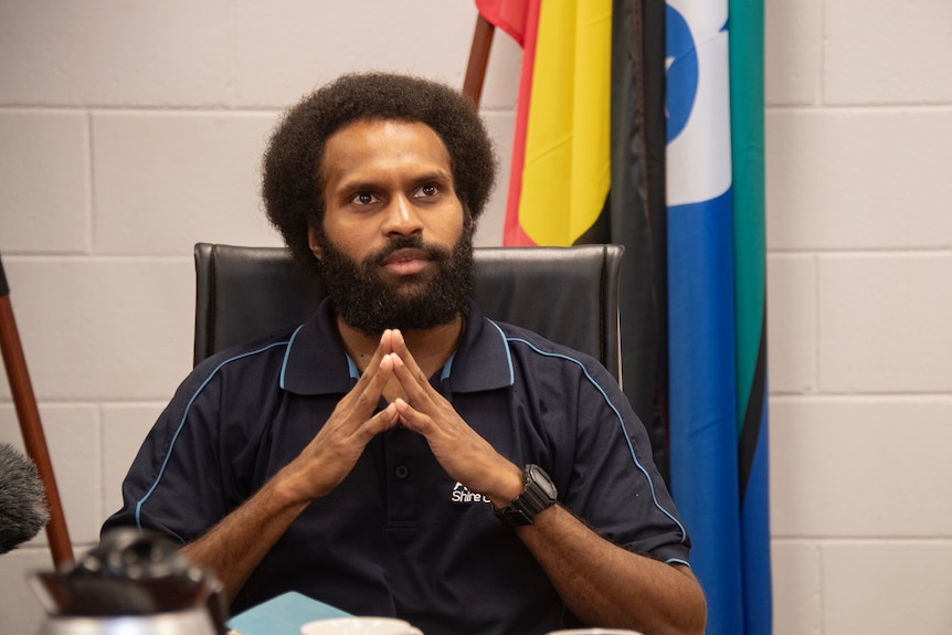 Kemuel Tamwoy sits in from of Aboriginal and Torres Strait Islander flags