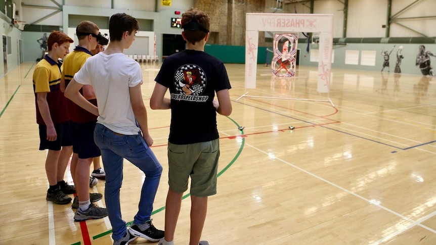 A group of people race drones inside a sports hall