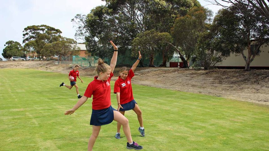 A boy runs with a football while two girls do handstands on green grass.