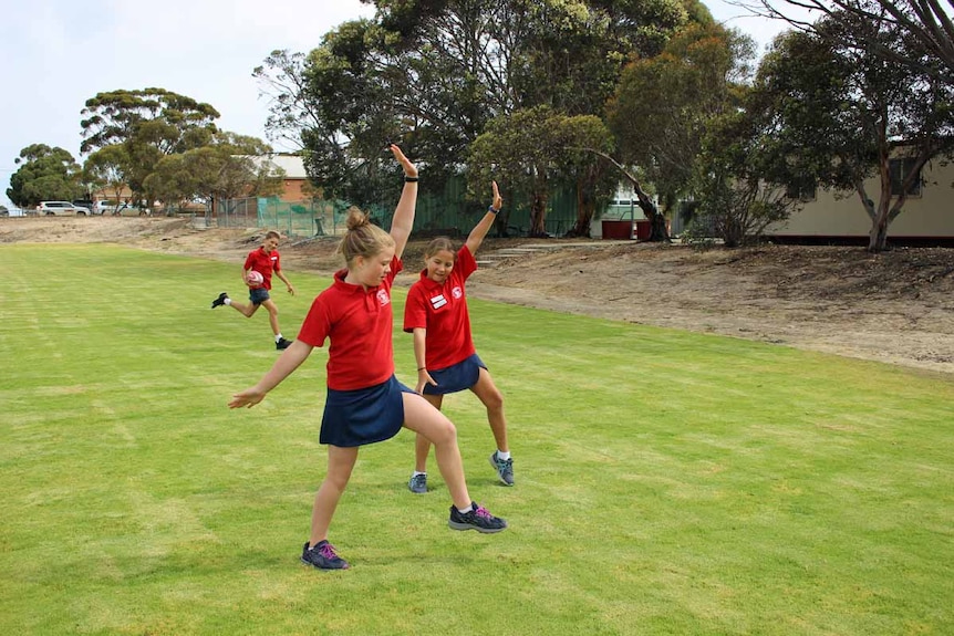 A boy runs with a football while two girls do handstands on green grass.