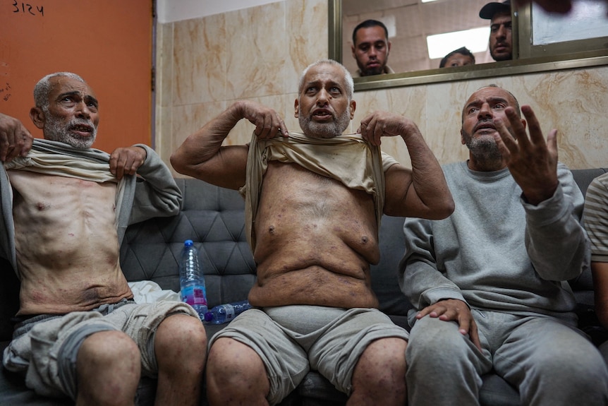 Three Palestinina prisoners holding up their shirts to reveal their stomachs sunken in after prison release.