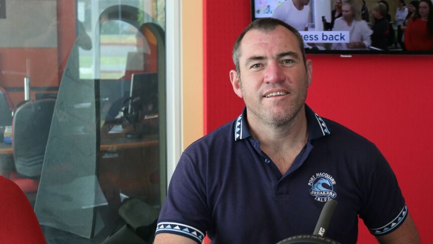 A man sitting down, wearing a dark blue polo shirt and smiling.