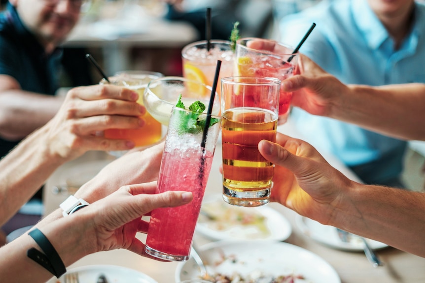 Close up of hands cheering with alcoholic drinks depicting friendship networks built overseas and at home.