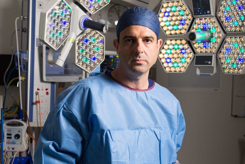 A mid-shot of AMA president Omar Khorshid standing in an operating theature with scrubs on and holding a face visor.