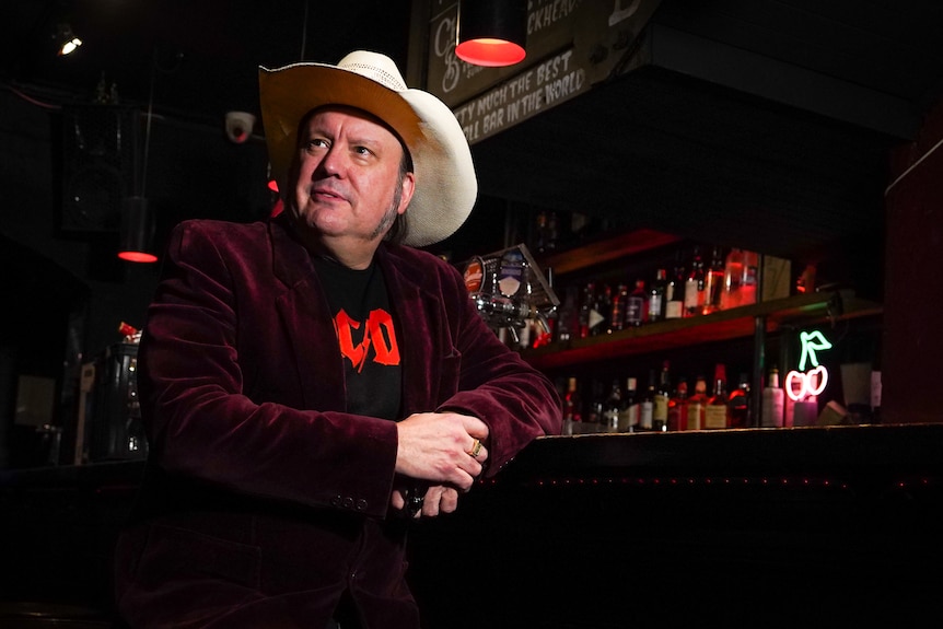 A man in a cowboy hat leaning on a bar.