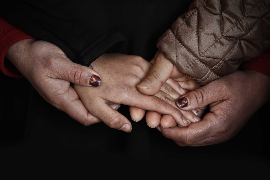 Close up of hands from three people holding each other depicting the support that sitting with grief can offer a sufferer.