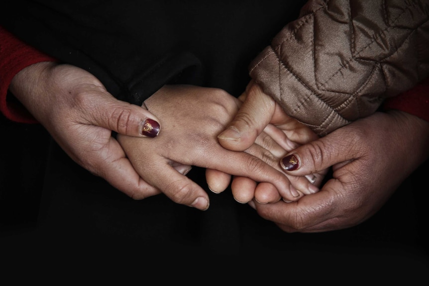 Close up of hands from three people holding each other depicting the support that sitting with grief can offer a sufferer.