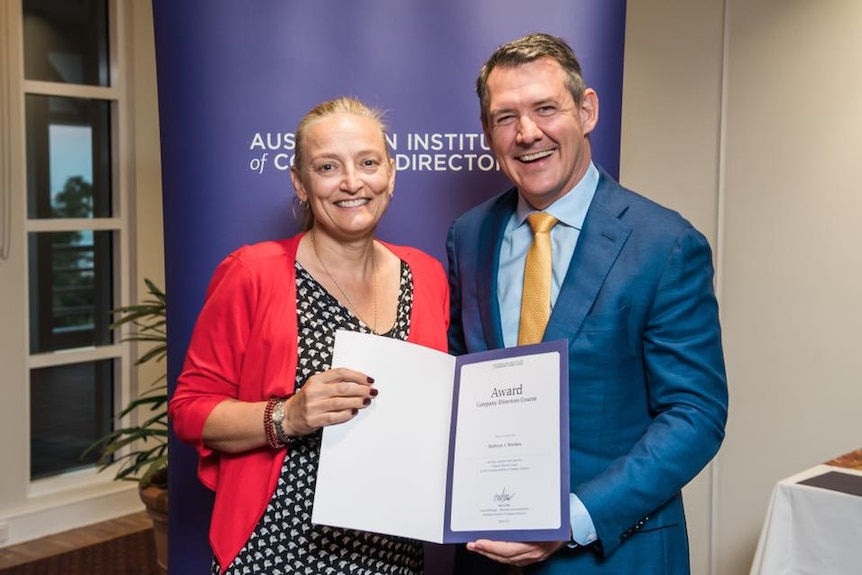 Kate Worden smiles as she holds her certificate beside Michael Gunner