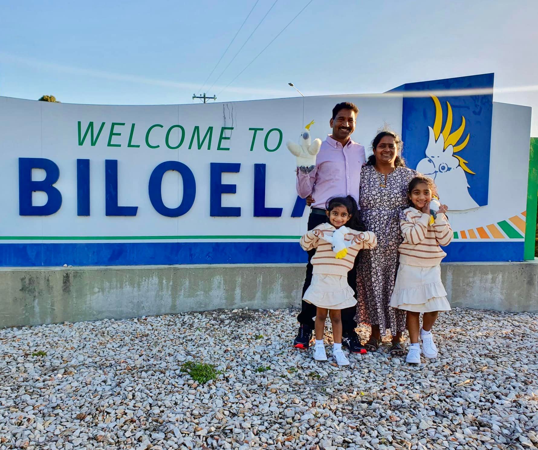 The four members of the Nadesalingam family stand in front of the Welcome to Bilo sign