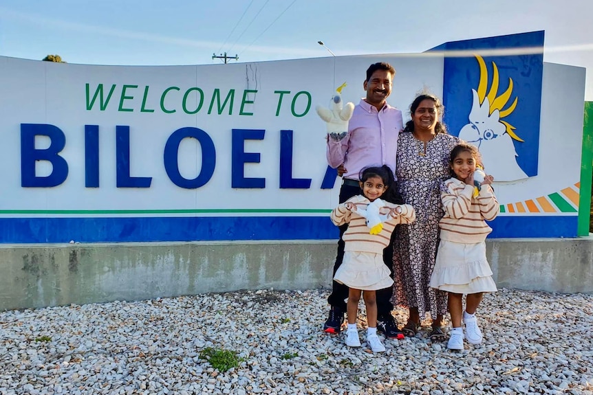 The four members of the Nadesalingam family stand in front of the Welcome to Bilo sign