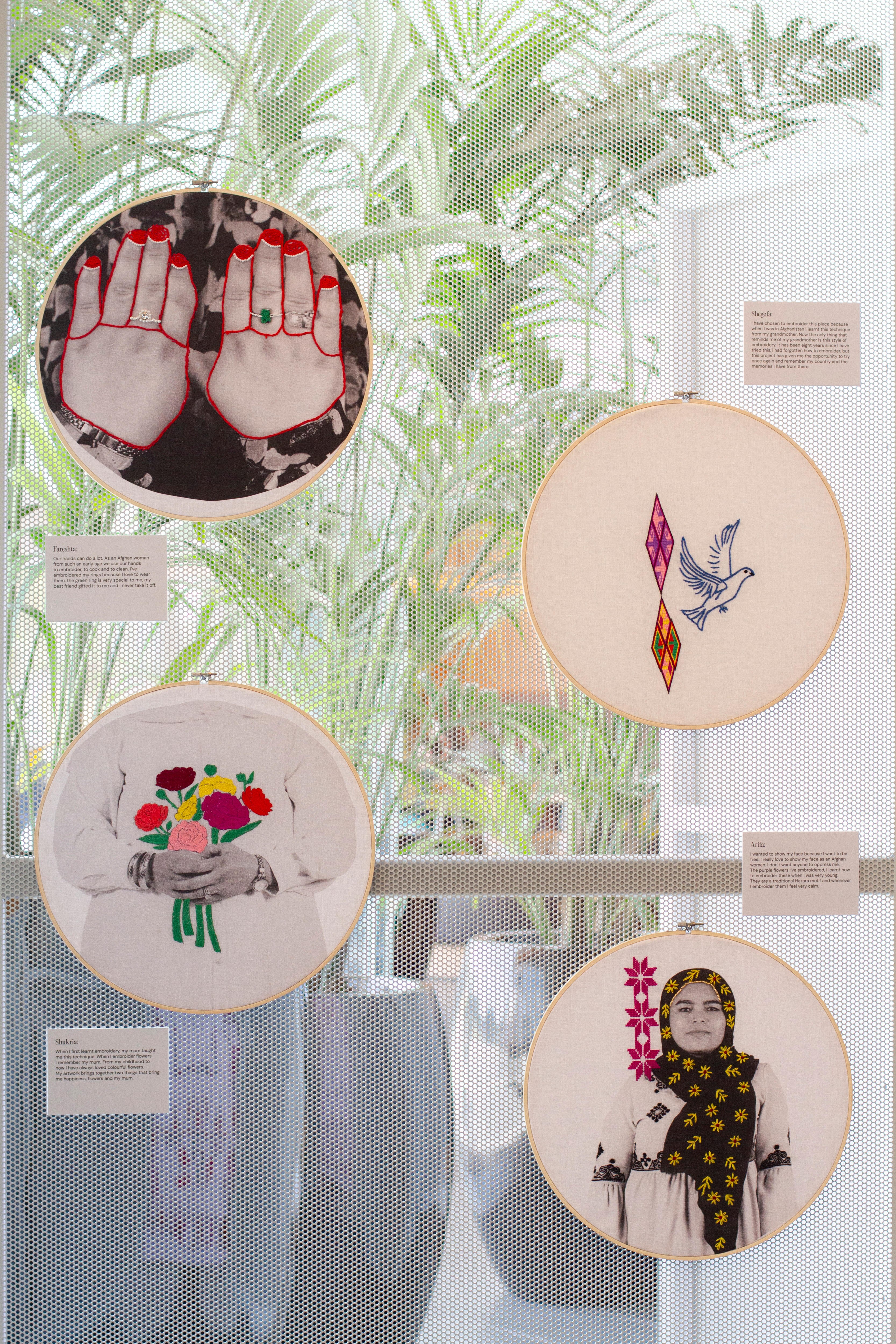 Photo of three round embroidery hoops hanging up with colourful patterns of flowers, birds and hands