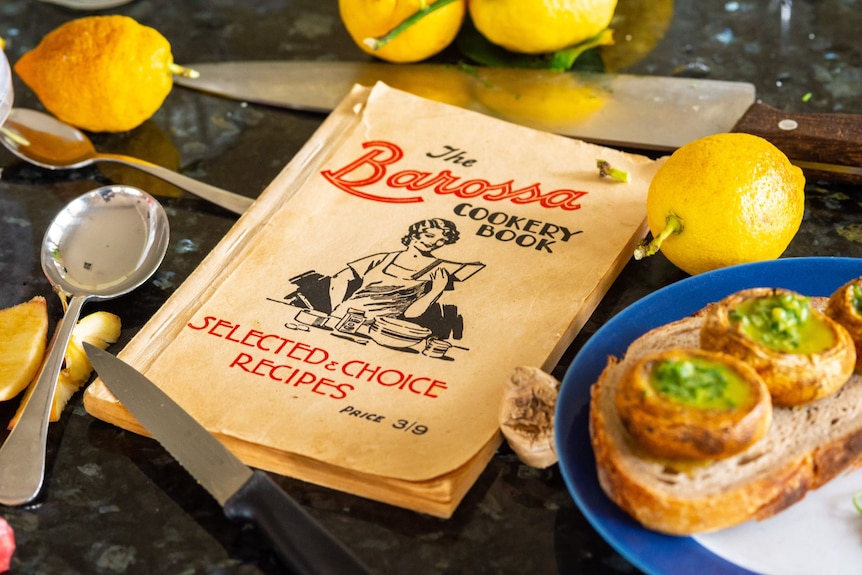 An old cookbook on a bench with lemons and cutlery next to it.