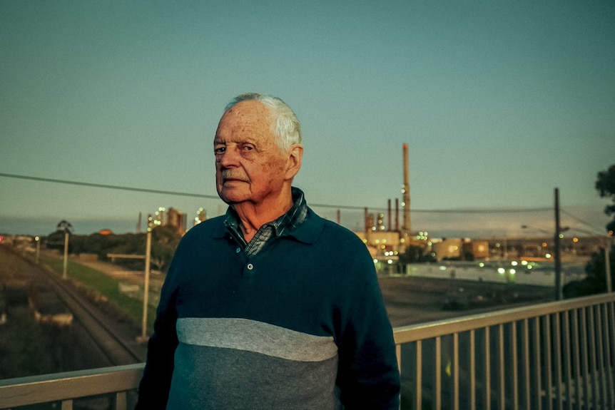 An elderly man standing in front of a fuel refinery.