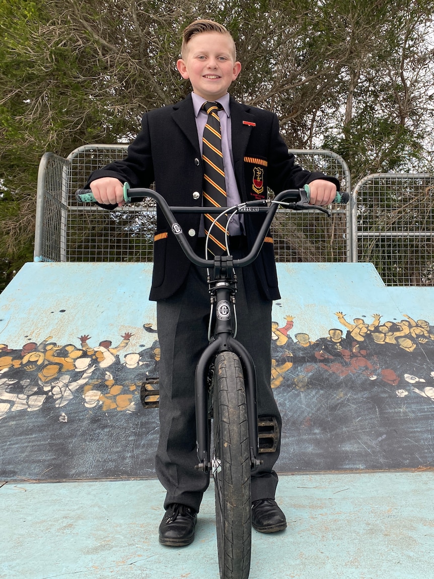 12-year-old student in uniform posing on bike looking at camera in skate park.
