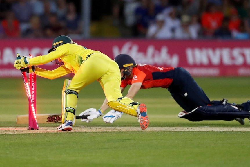 A wicketkeeper breaks the stumps as the batter slides to make her ground.