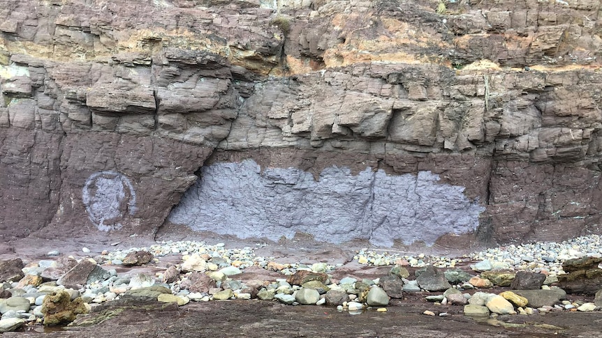 A patch of grey-coloured paint on a rock wall at the bottom of a cliff