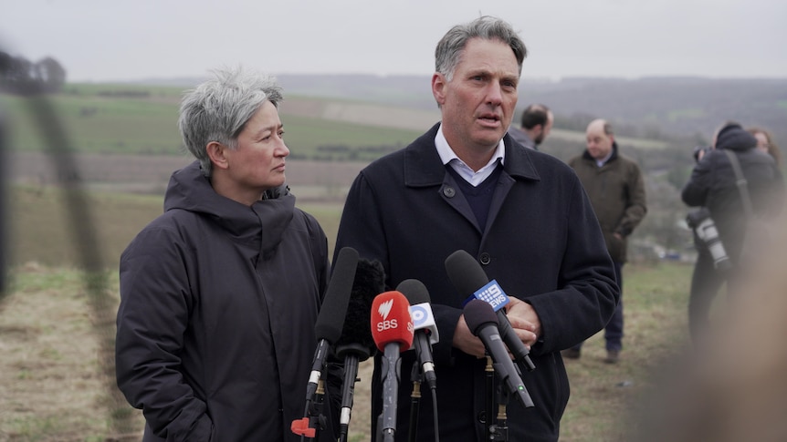 Wong, right, looks at Marles, left, who is speaking. They stand in a field wearing heaving jackets.