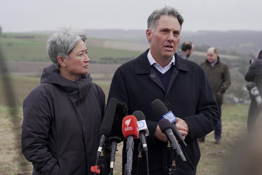 Wong, right, looks at Marles, left, who is speaking. They stand in a field wearing heaving jackets.