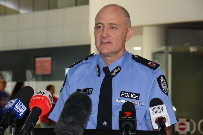 A man wearing a police uniform stands in front of a bank of microphones.