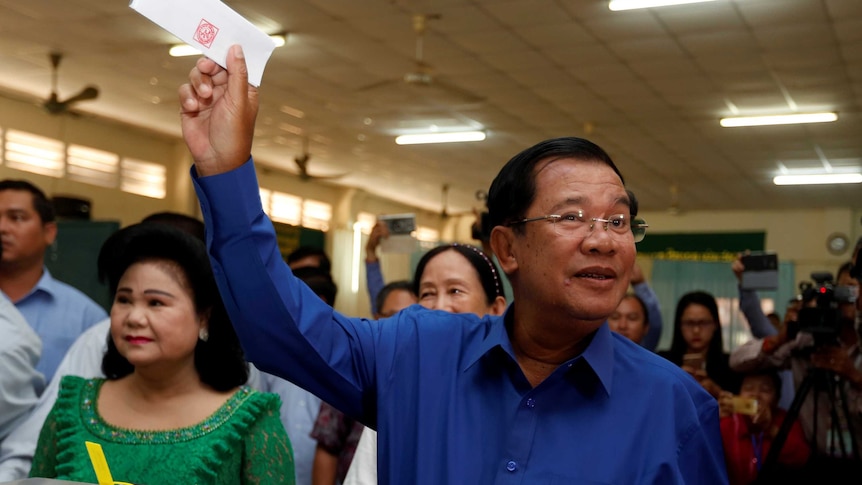 Hun Sen holds up his voting card while standing in front of a crowd at a voting booth.