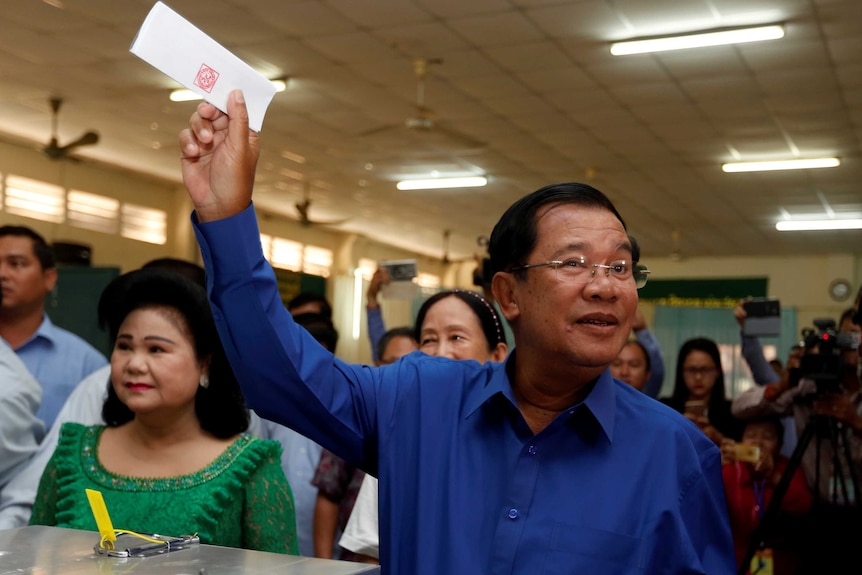 Hun Sen holds up his voting card while standing in front of a crowd at a voting booth.