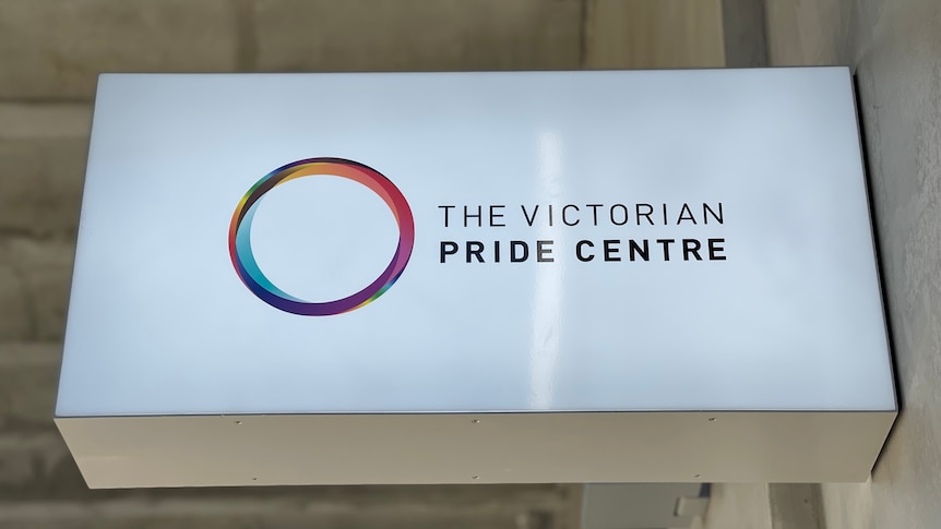 A white sign with 'Pride Centre' written on it and a rainbow coloured circle symbol signifies the entrance to a new building.