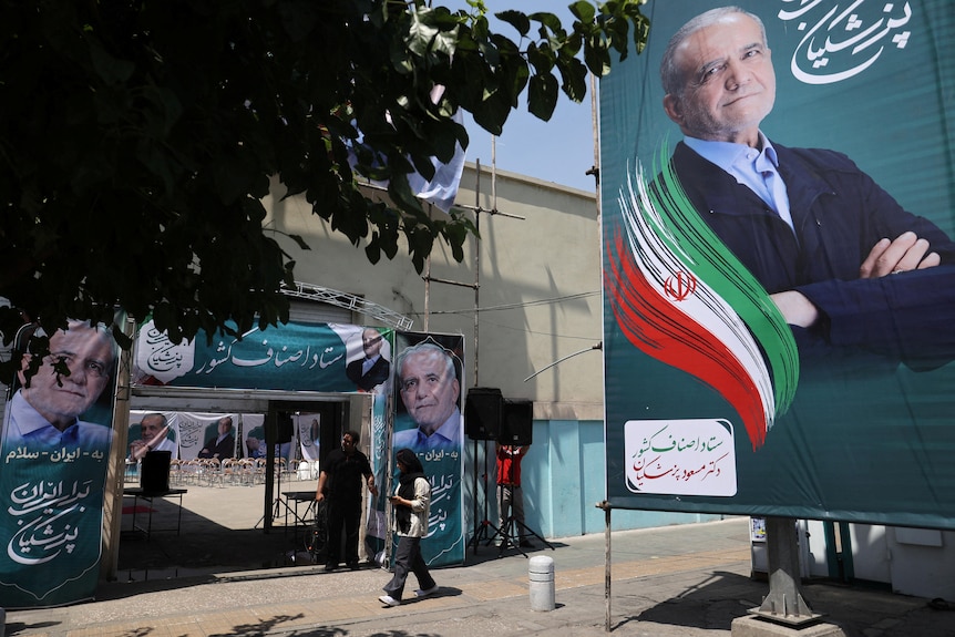 A large green banner of a smiling man in a suit hangs beside an Iranian street.