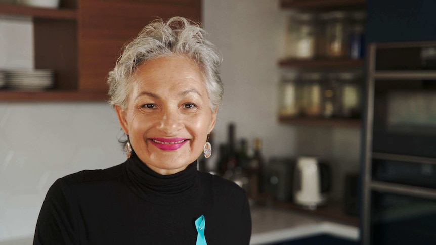 A portrait photo of a woman smiling, wearing a black top and bright lipstick