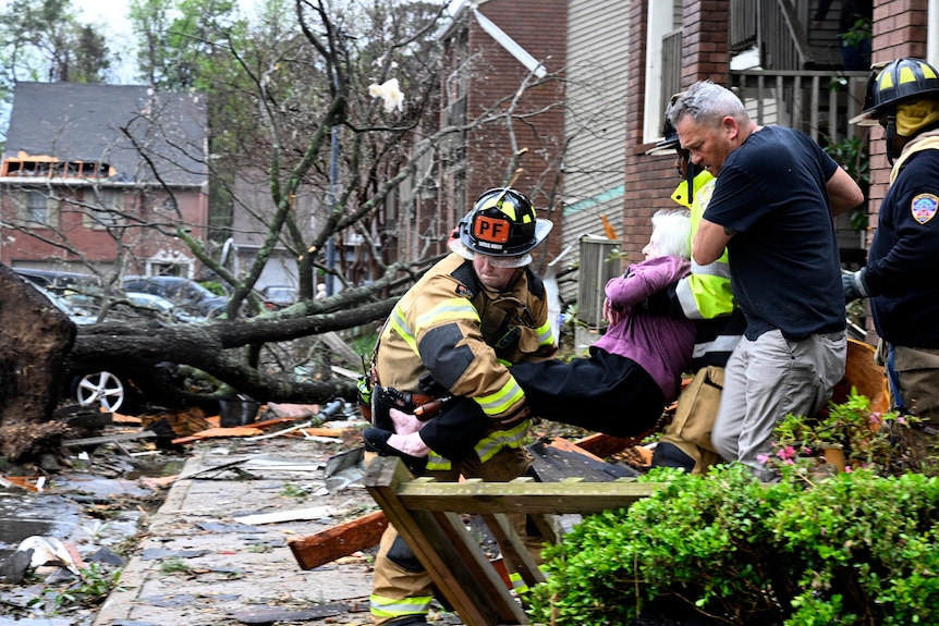 Firefighters carry an elderly woman out of her home as a tree is shown knocked over in the background
