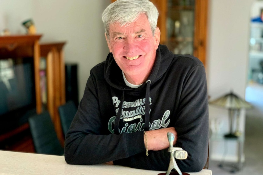 A man with a black jumper and silver hair poses smiling withy a Logie award