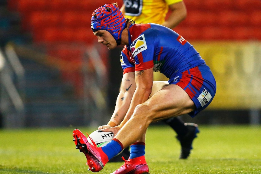 A Newcastle Knights NRL player grounds the ball as he scores a try against the Wests Tigers.