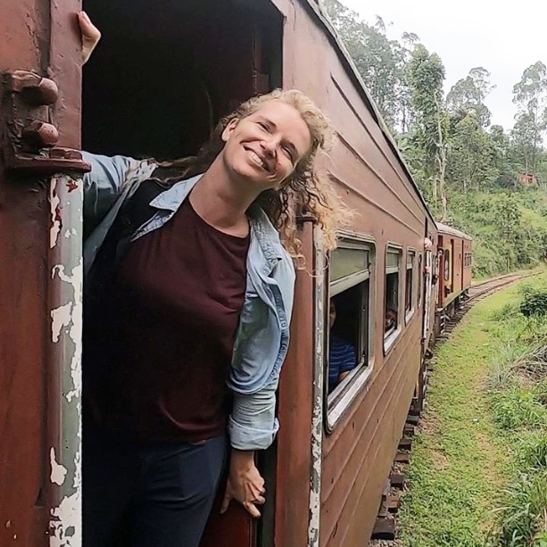 Young woman hanging out of train doorway in Sri Lanka.