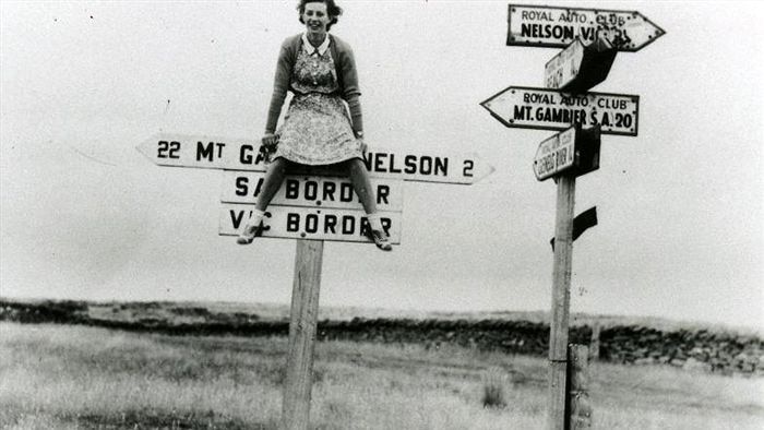 A black and white photo of a woman sitting on the marker for the SA/Victoria border.
