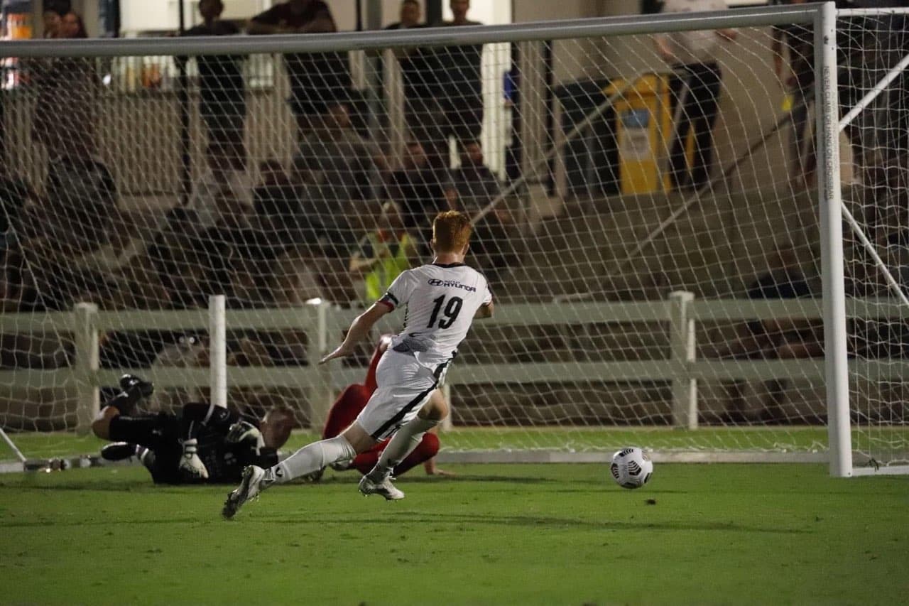 a player in a white and black jersey kicks a ball into a goal