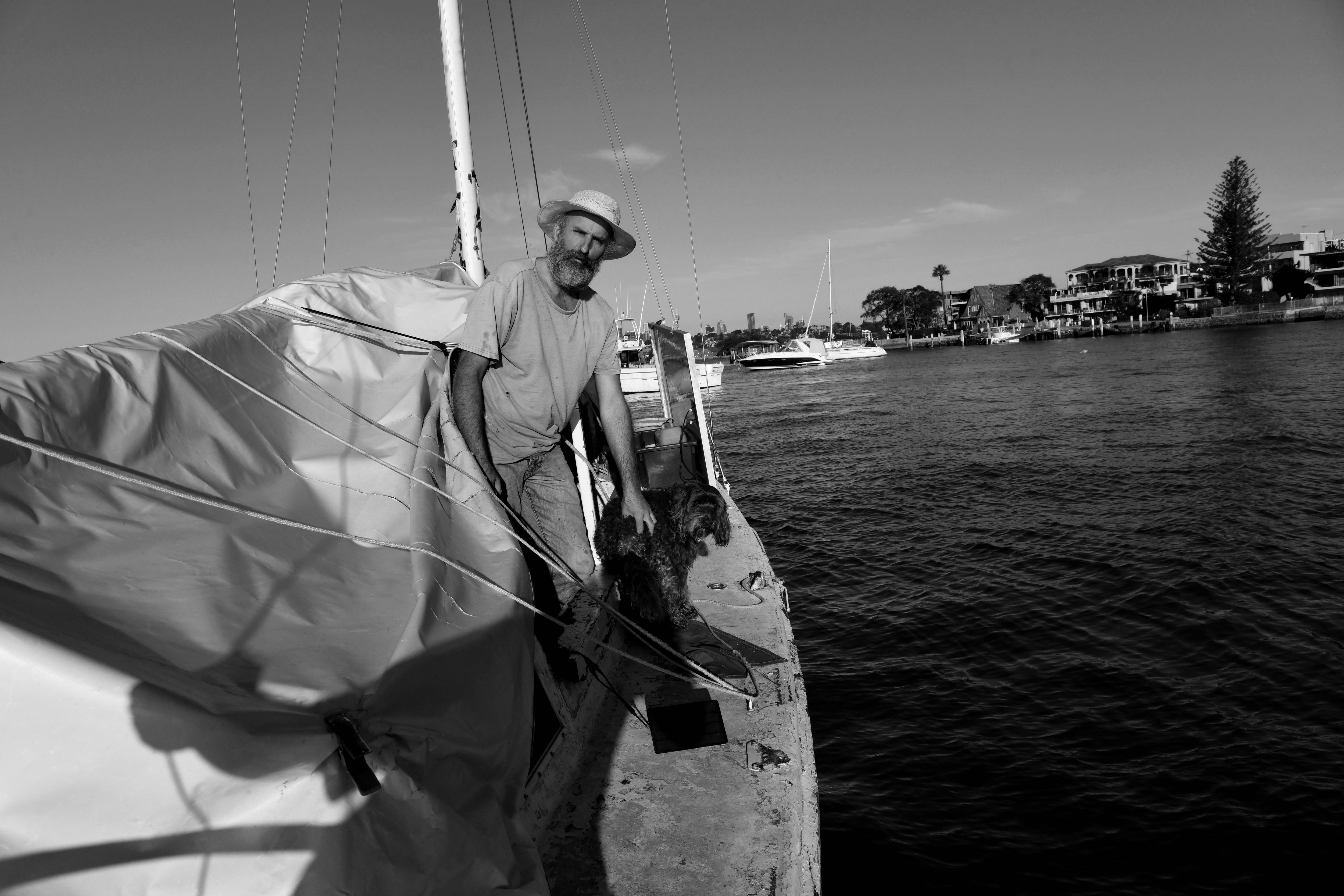 A man holds back a dog with both looking at the camera. They stand on a yacht