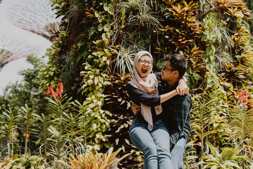 A man holds his wife in his arms, who is exclaiming with joy