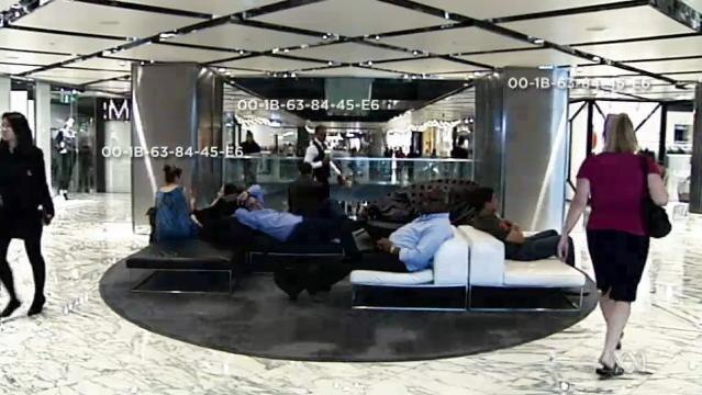 People walk through shopping centre, coded numbers superimposed on screen