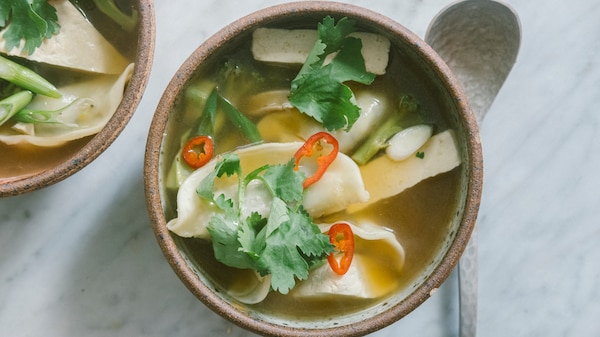 A bowl of dumpling soup with broccoli and tofu topped with coriander and sliced chilli.