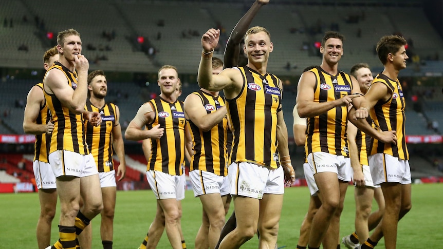 Multiple Hawthorn Hawks players walk together at Docklands Stadium, smiling after an AFL win.