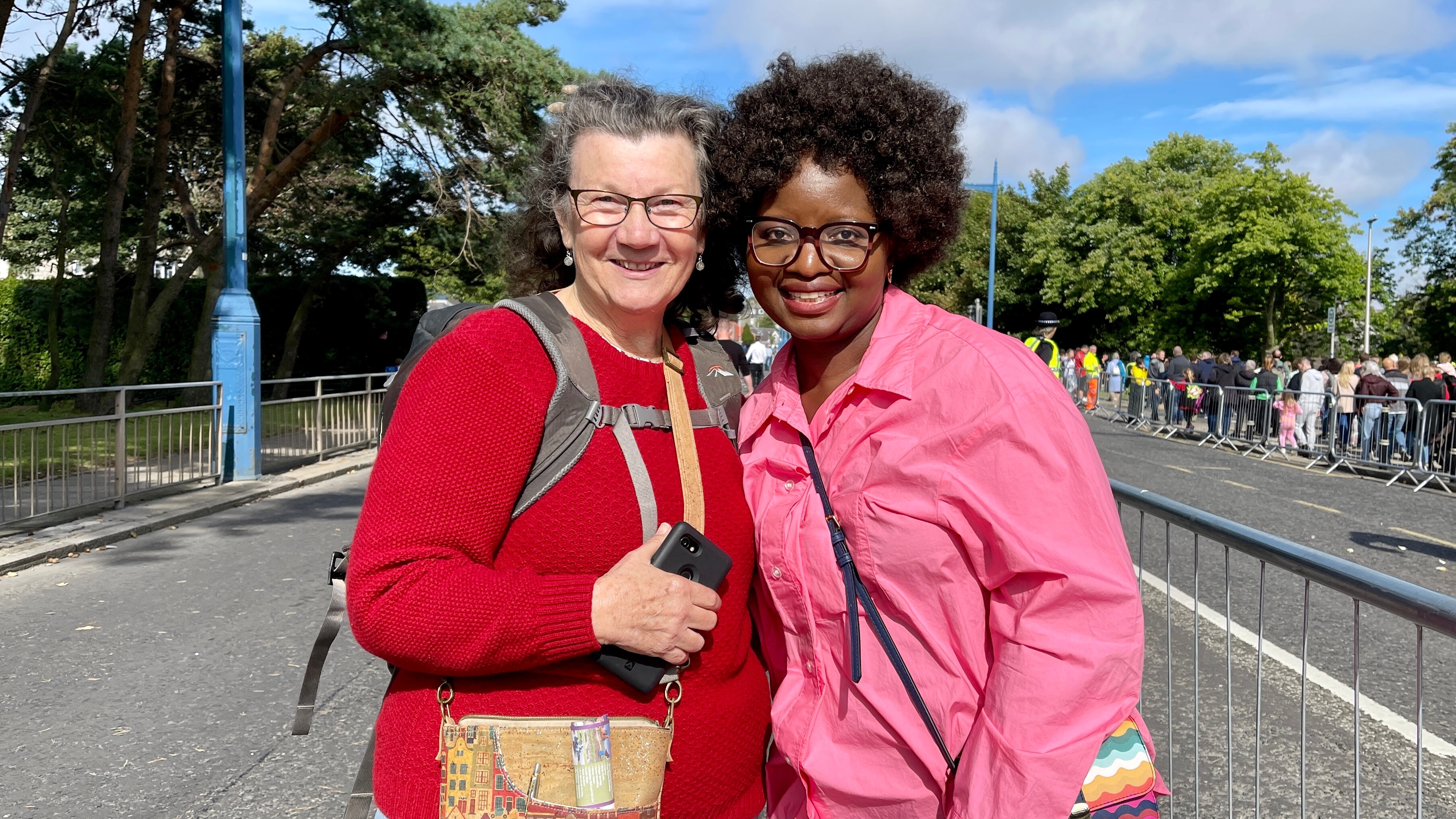 A white woman and a black woman pose smiling together by a barricade. 