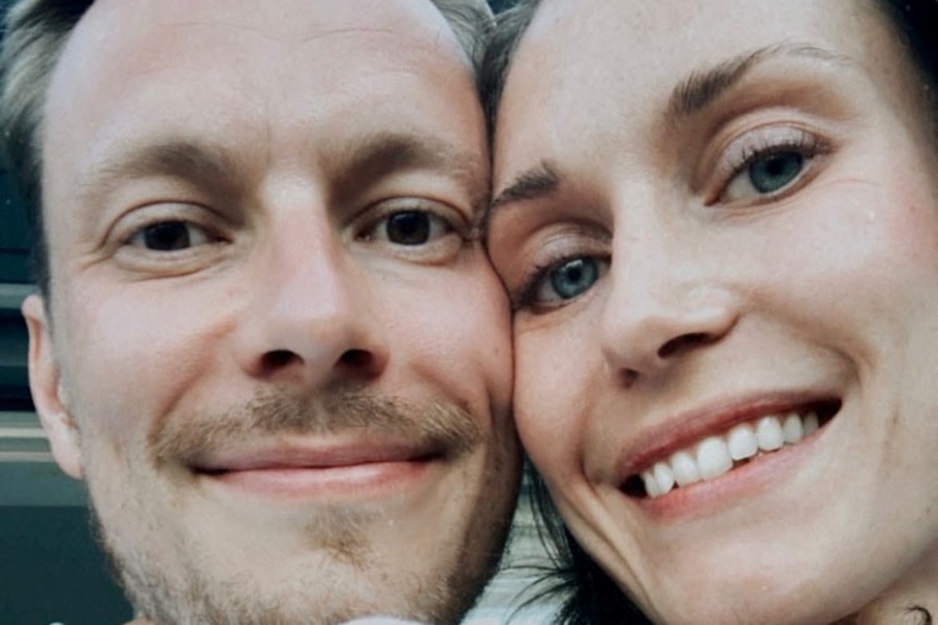 Sanna Marin and husband Markus Raikkonen with their cheeks pressed against each other. They are a white and in their 30s.3