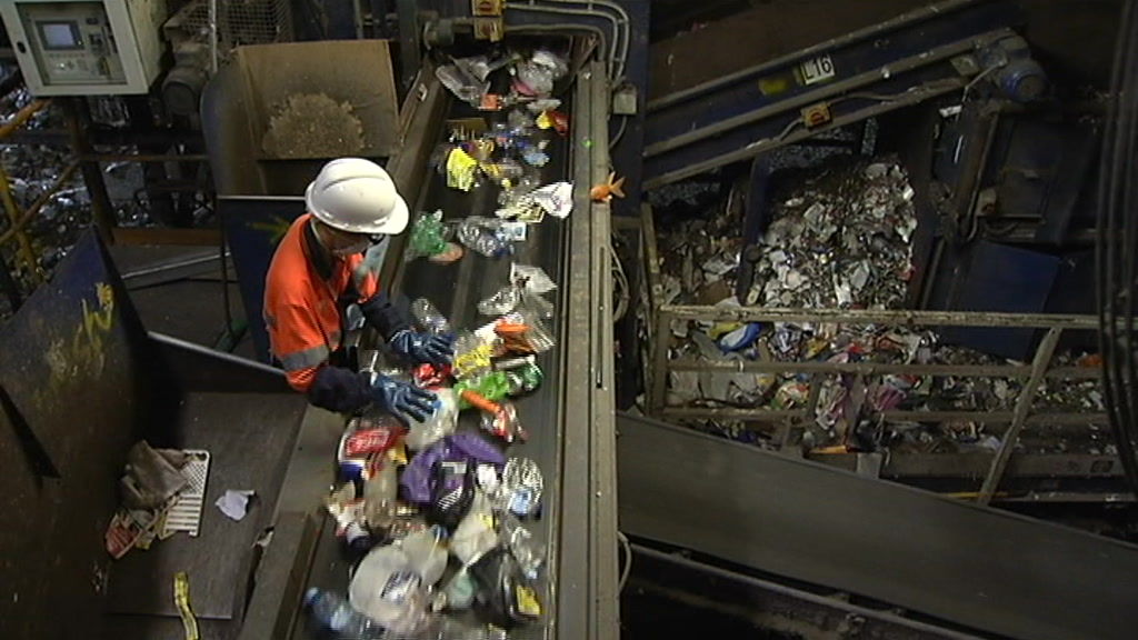 An anonymous worker sorts through plastic items on a conveyor belt