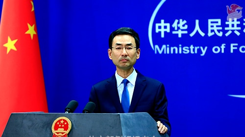 China's foreign ministry spokesperson Geng Shuang stands in front of a podium and next to a Chinese flag.