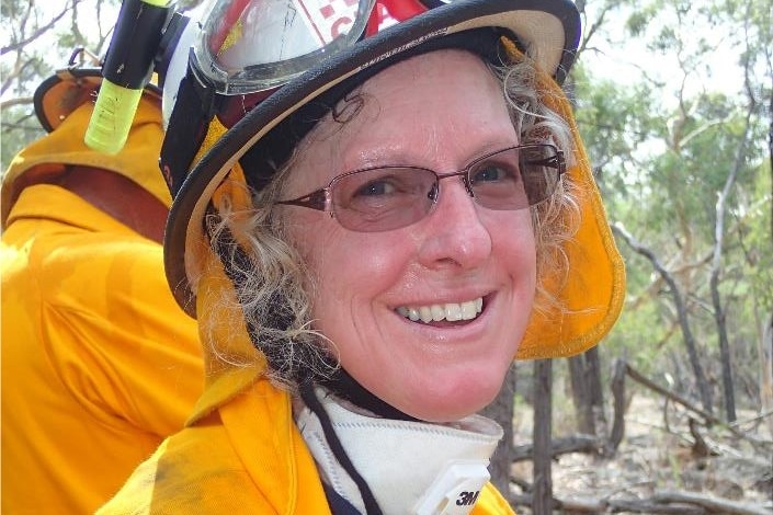 A woman in a firefighting uniform holds a water bottle and smiles.